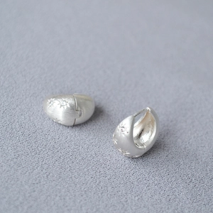 Macro view of silver hoop earrings with brushed texture and star engraved zircons