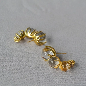Close-up of golden C-shaped earrings with transparent glass beads in a curved layout
