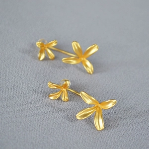 Macro shot of matte gold floral earrings with a textured finish on a grey fabric background