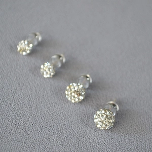 Close-up of four sparkling silver ball stud earrings with rhinestones on grey fabric