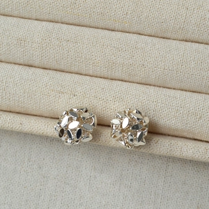 Macro shot of silver faceted hollow ball stud earrings on a textured beige display