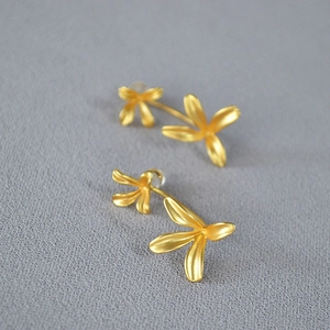 Macro shot of matte gold floral earrings with two four-petal flowers on textured background