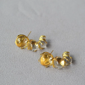 Macro shot of three clear glass spheres in gold claw settings on C-shaped earrings