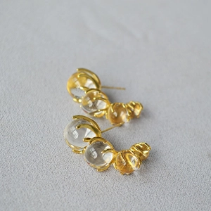 Close-up of golden C-shaped earrings with transparent gradient glass beads on dark background