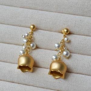 Close-up of matte gold lily of the valley earrings with white pearls on a jewelry tray