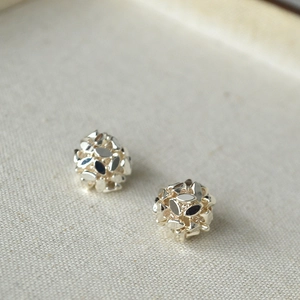 Macro shot of silver hollow cut-out sphere stud earrings on a textured linen background