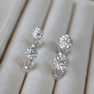 Macro detail of 925 silver needle stud earrings with pave crystals on beige velvet tray