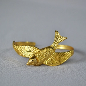 Macro detail of a 3D flying swallow on a vintage brass gold-plated adjustable cuff bracelet