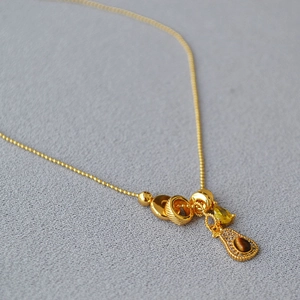 Detail of vintage gold necklace with tiger eye stone and yellow drop charm on grey fabric