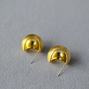 Macro detail of gold brushed hollow hemisphere earrings with polished mirror interior finish