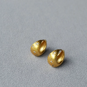 Detail of matte gold star huggie earrings with brushed texture and zircon stones