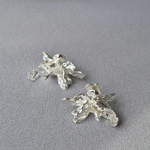 Vue macro de boucles d'oreilles irrégulières en métal liquide argenté sur tissu gris