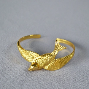 Golden open cuff bracelet featuring a lifelike 3D swallow design on a textured background