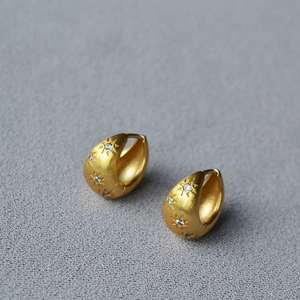 Macro detail of matte gold star earrings with brushed texture and zircon inlay