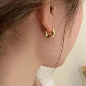Close-up of a model wearing a thick golden teardrop earring with a minimalist design