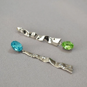 Detail of silver wavy earrings with blue and green oval gemstones on grey fabric