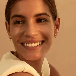 Close-up of small gold bubble hoop earrings with intricate hollow design on model