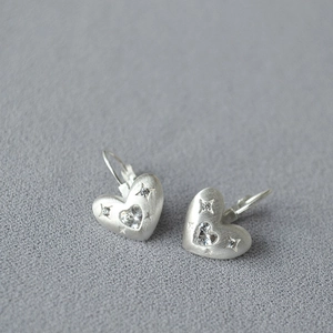 Vue macro de boucles d'oreilles cœur argenté brossé avec zircon central et détails gravés