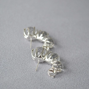 Detail view of silver C-shaped earrings with clear gradient glass beads on gray fabric