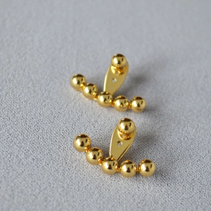 Primer plano de pendientes de latón chapado en oro con diseño de cuentas curvas y elegantes
