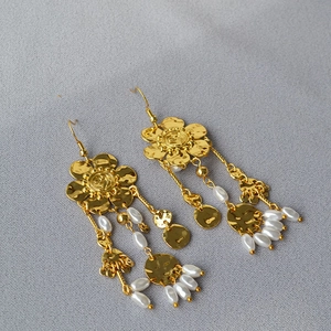 Golden flower earrings with hanging pearl tassels on a textured grey background