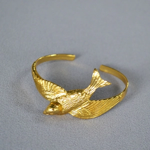 Detailed close-up of a 3D flying swallow open cuff bracelet in gold-plated brass finish