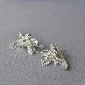 Vue macro des boucles d'oreilles fleur 3D argentées irrégulières avec surface miroir polie