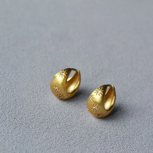 Close-up of golden brushed metal earrings with sparkling star-shaped zircon insets