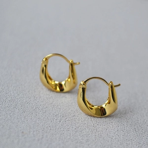 Macro shot of minimalist gold-plated U-shaped earrings with a twisted metal design