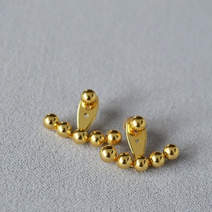 Primer plano macro de pendientes minimalistas de latón dorado con diseño de cuentas