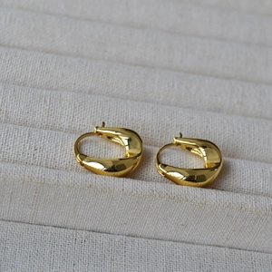 Detail of twisted gold earrings with mirror polish finish on beige jewelry tray