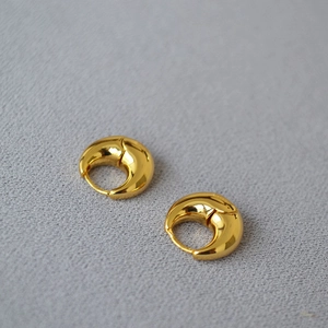 Macro detail of French design thick crescent gold plated brass earrings on grey fabric