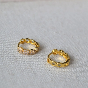 Detail of gold hoop earrings with white zircon clusters on a soft cream fabric