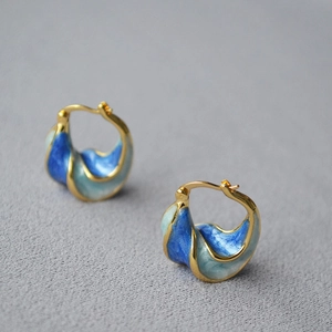 Macro view of artistic spiral gold earrings with blue marbled enamel on grey fabric