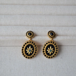 Macro detail of retro gold earrings with black enamel disks and star motif charms