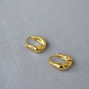 Close-up of irregular U-shaped gold earrings with polished finish on grey fabric background