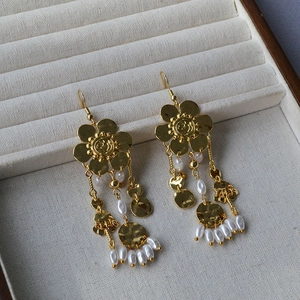 Macro detail of gold flower earrings featuring pearl tassels and hammered metal discs