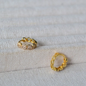 Close-up of gold flower hoop earrings with white and purple zircon on beige fabric
