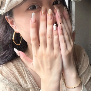 Neutral almond press-on nails with gold leaf accents and chic irregular hoop earrings