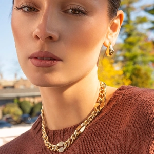 Detail shot of chunky gold chain necklace and water drop earrings on model in sunlight