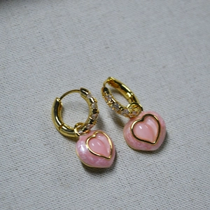 Gros plan de boucles d'oreilles cœur en émail rose et zircons sur tissu gris