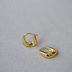 Detailed view of polished gold U-shaped twisted earrings on light gray texture