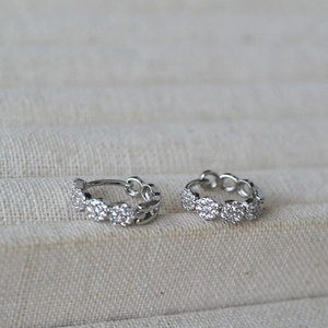 Macro shot of silver pavé crystal huggie hoop earrings with circular stone clusters