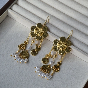 Detailed close-up of gold flower earrings with pearl tassels and hammered metal discs
