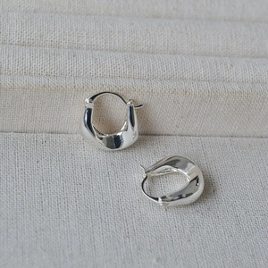 Detail of silver irregular U-shaped earrings on textured beige fabric background