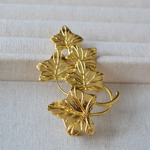 Vintage golden vine leaf brooch with detailed veins on a beige jewelry display tray