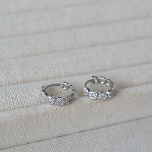 Macro shot of silver pavé crystal hoop earrings on a beige velvet jewelry display stand