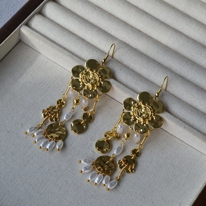 Detailed macro view of golden floral earrings with dangling pearl tassels and chain fringe