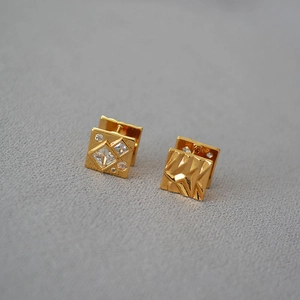 Detail of asymmetrical gold plated square stud earrings with zircon inlay and textured surface