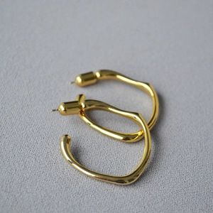 Detailed view of large irregular golden hoop earrings with high-polish metallic finish